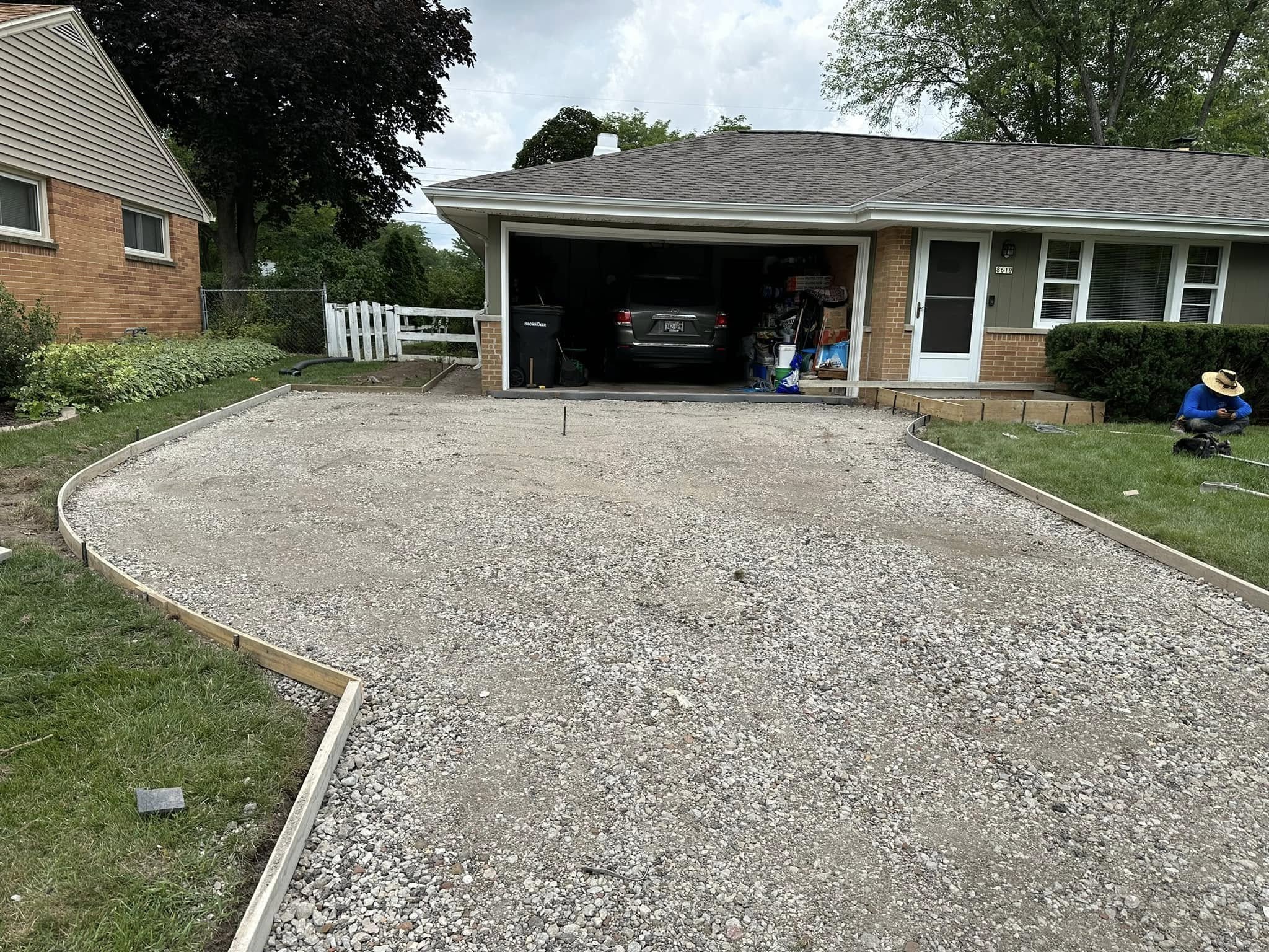 Gravel sub-base and wooden concrete forms set along driveway edges in front of brick ranch home
